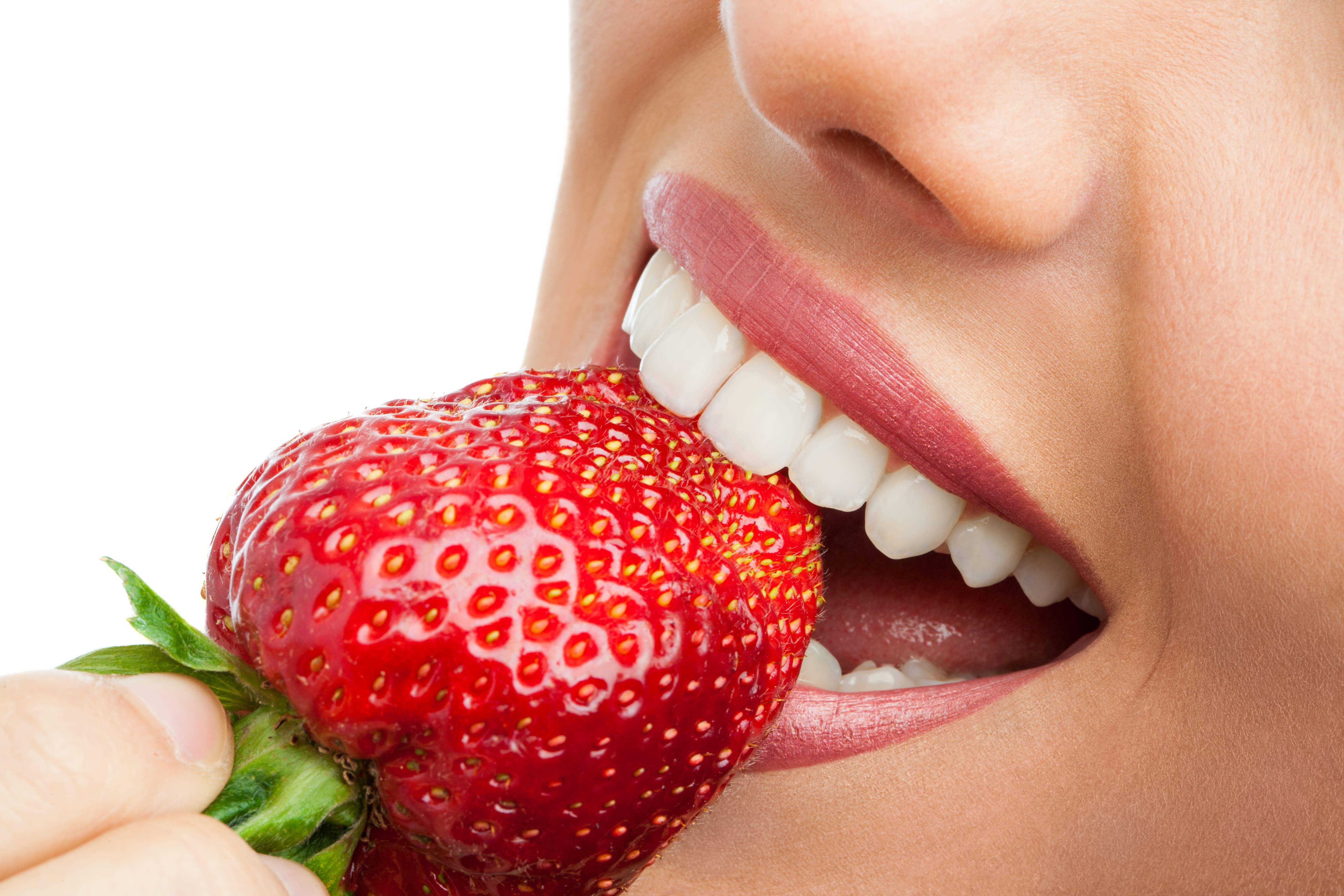 Close up of white teeth biting into a strawberry