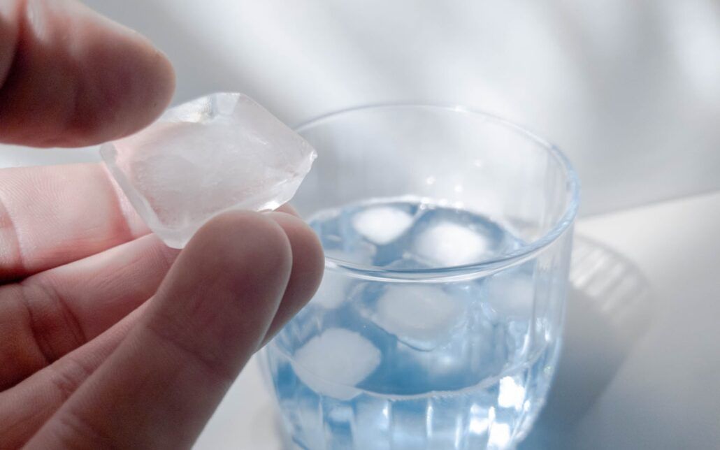 Cup filled with Water and Ice, with Hand holding Ice cube up close