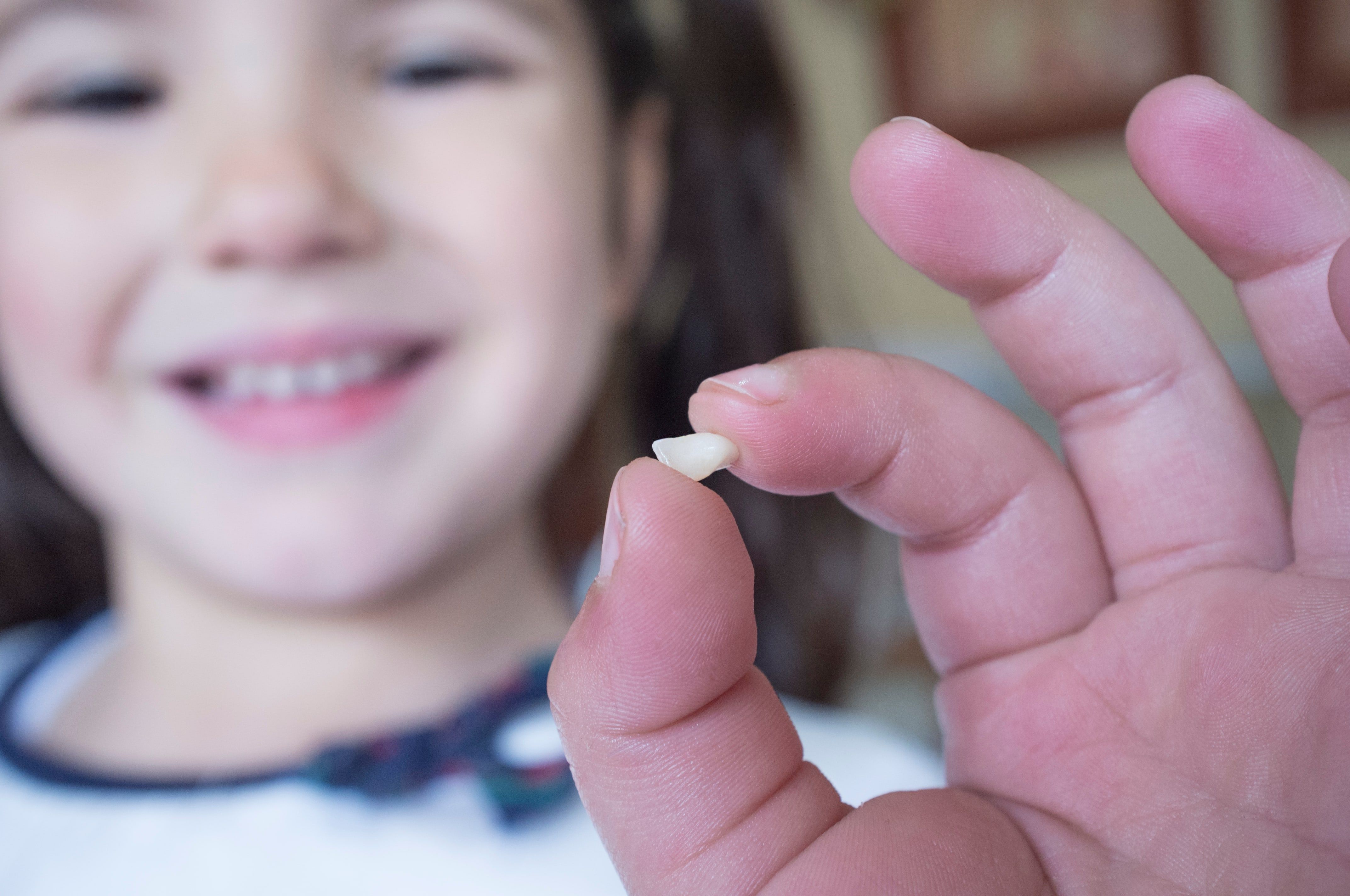 Picture of a very young girl smiling and holding her first lost tooth
