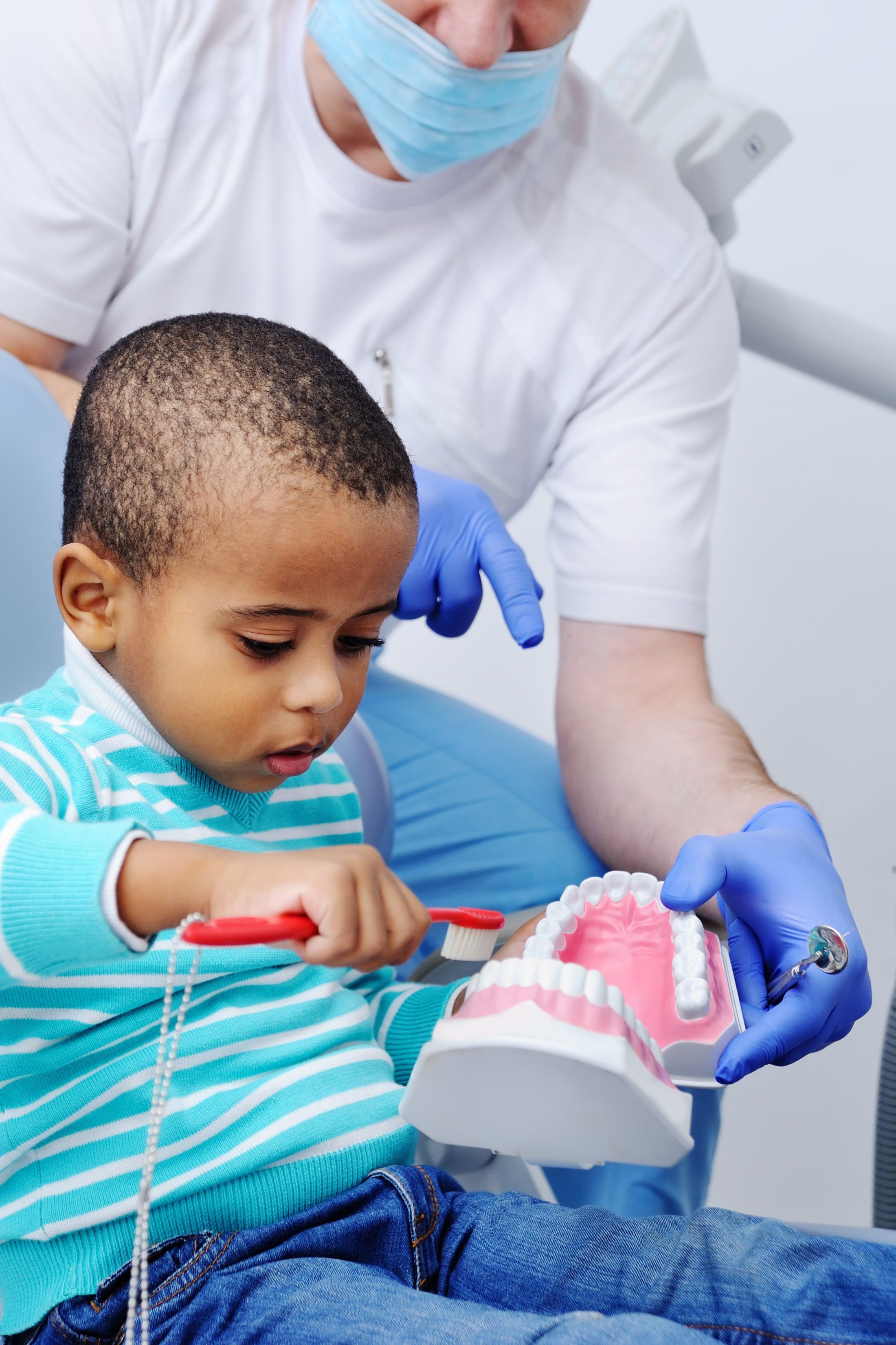 Pediatric dentist shows young child how to brush their teeth on an enlarged tooth model