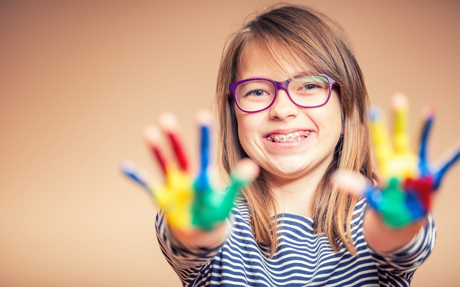 Child with braces and colored paint on hands